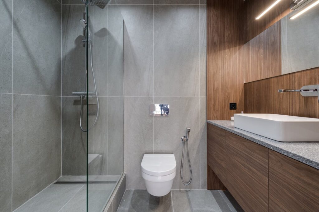 pexels-photo-7614405 Elegant modern bathroom featuring a walk-in shower, sink, and toilet with a stylish wooden finish.
